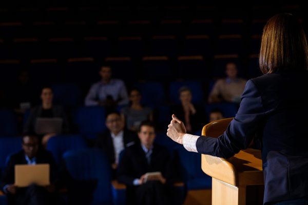 Rear view of female business executive giving a speech at conference center